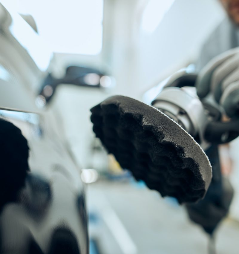 Close-up worker polishing car at auto service workshop.