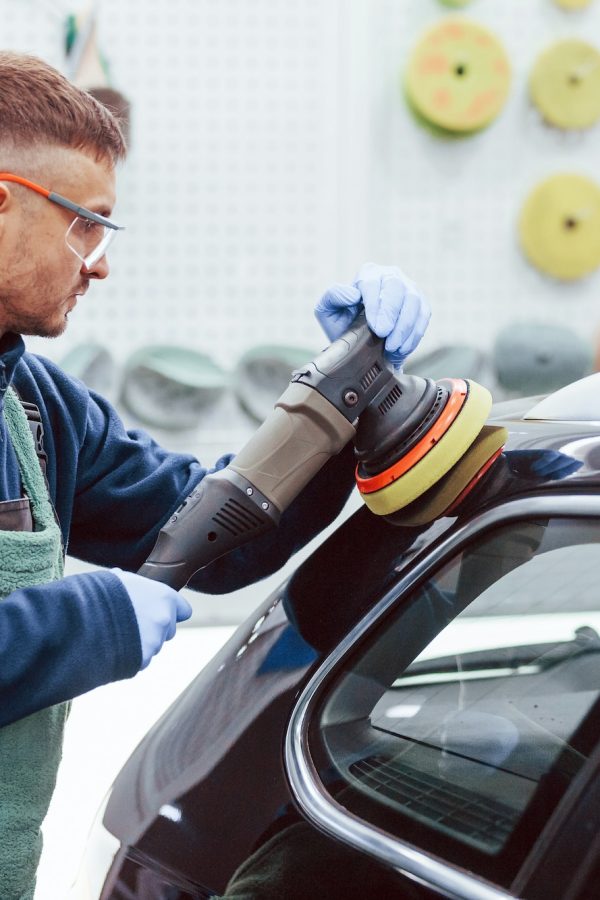 Male worker in uniform polishing new modern car. Conception of service